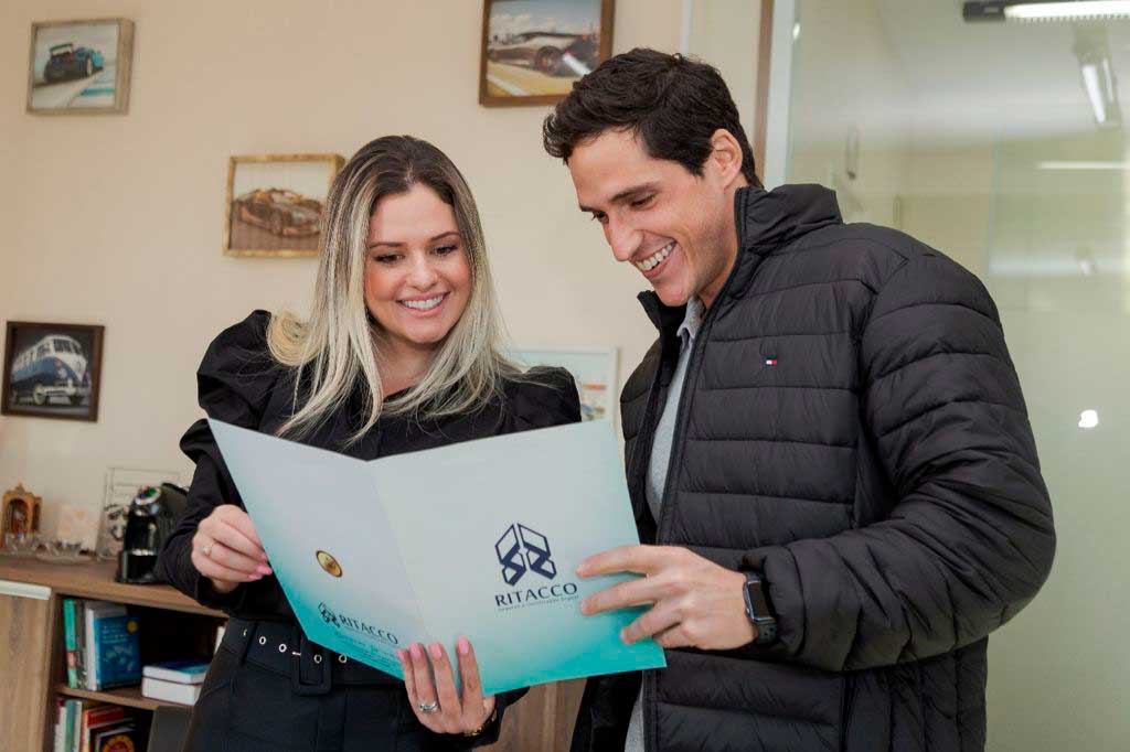Diretores do Grupo Ritacco lendo conteúdo da pasta com a marca do Grupo Ritacco estampada na capa.